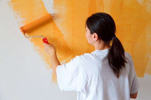 A woman painting the wall orange with a paint roller